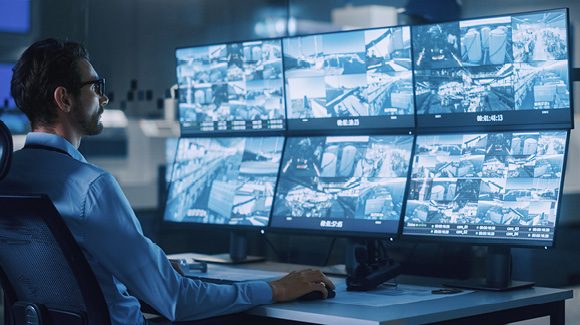A man sits at a desk with several monitors.
